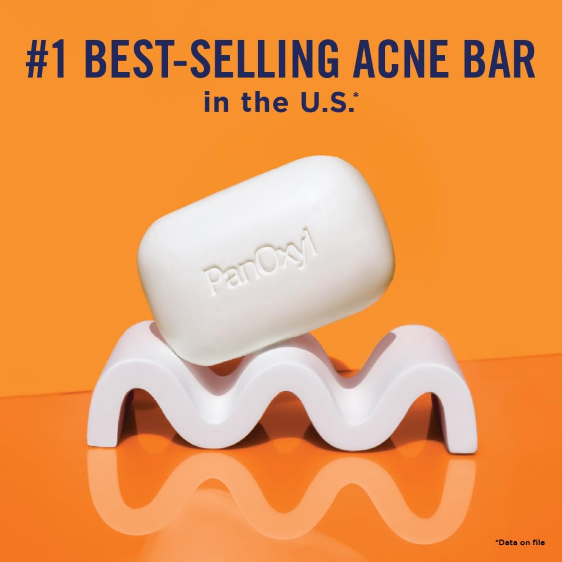 White acne bar on a wavy stand with 'PanOxyl' branding against an orange background