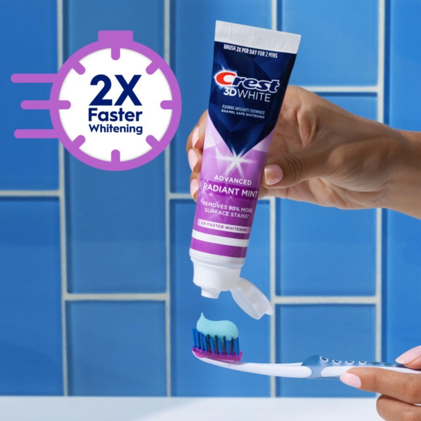 Crest 3D White toothpaste tube with a hand holding a toothbrush against a blue tiled background