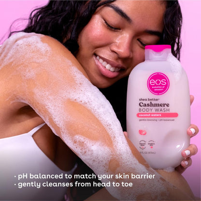 Woman with soap suds on her arm holding a bottle of eos Cashmere Body Wash against a pink background