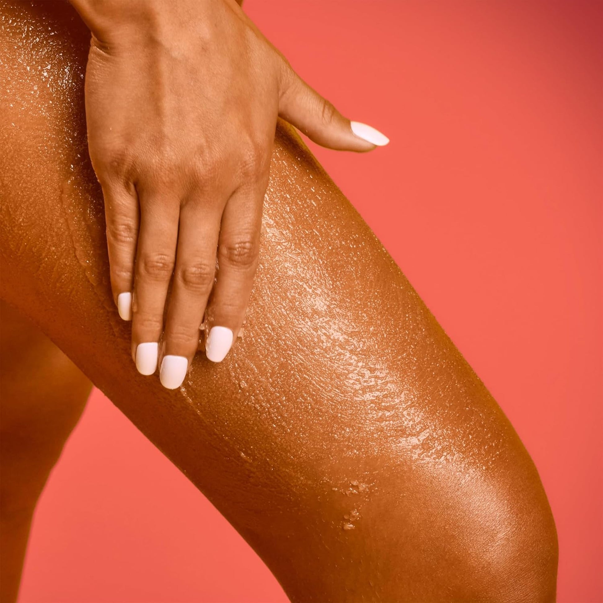 Hand applying a brown cosmetic product to a leg against a red background
