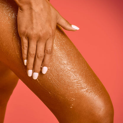 Hand applying a brown cosmetic product to a leg against a red background