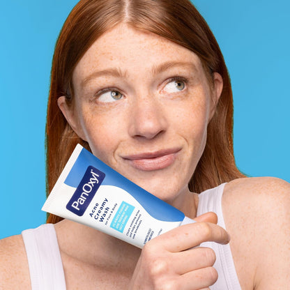 Woman holding a tube of Pan-O-Me Acne Creamy Wash against a blue background