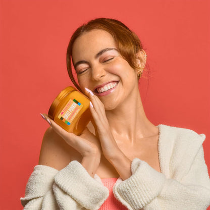Woman applying a jar of cosmetic product to her face against a red background