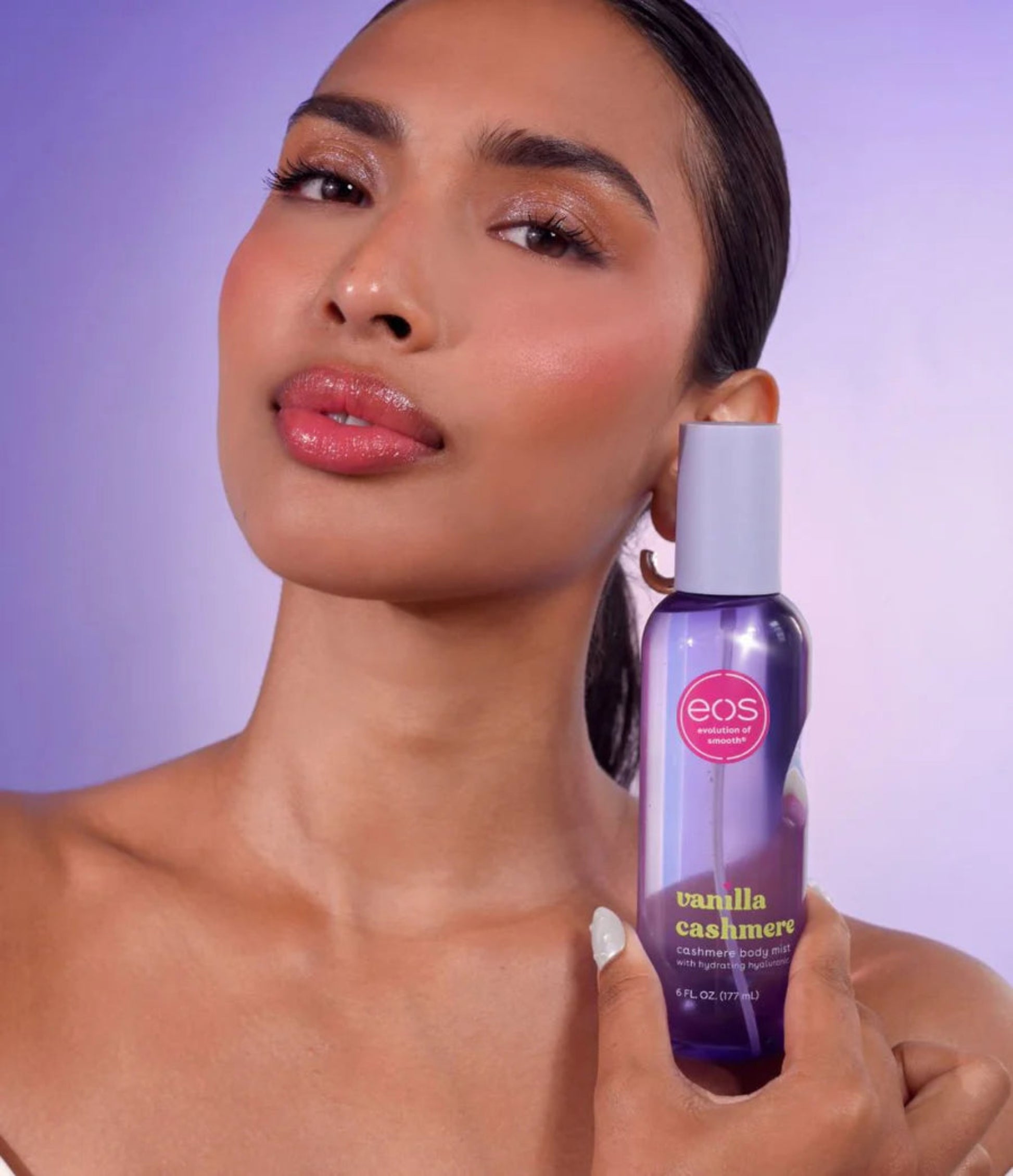 Woman holding an eos vanilla cashmere body spray against a purple background