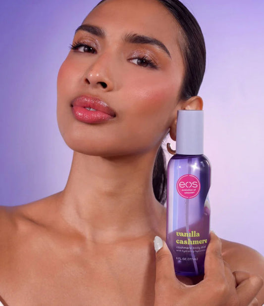 Woman holding an eos vanilla cashmere body spray against a purple background