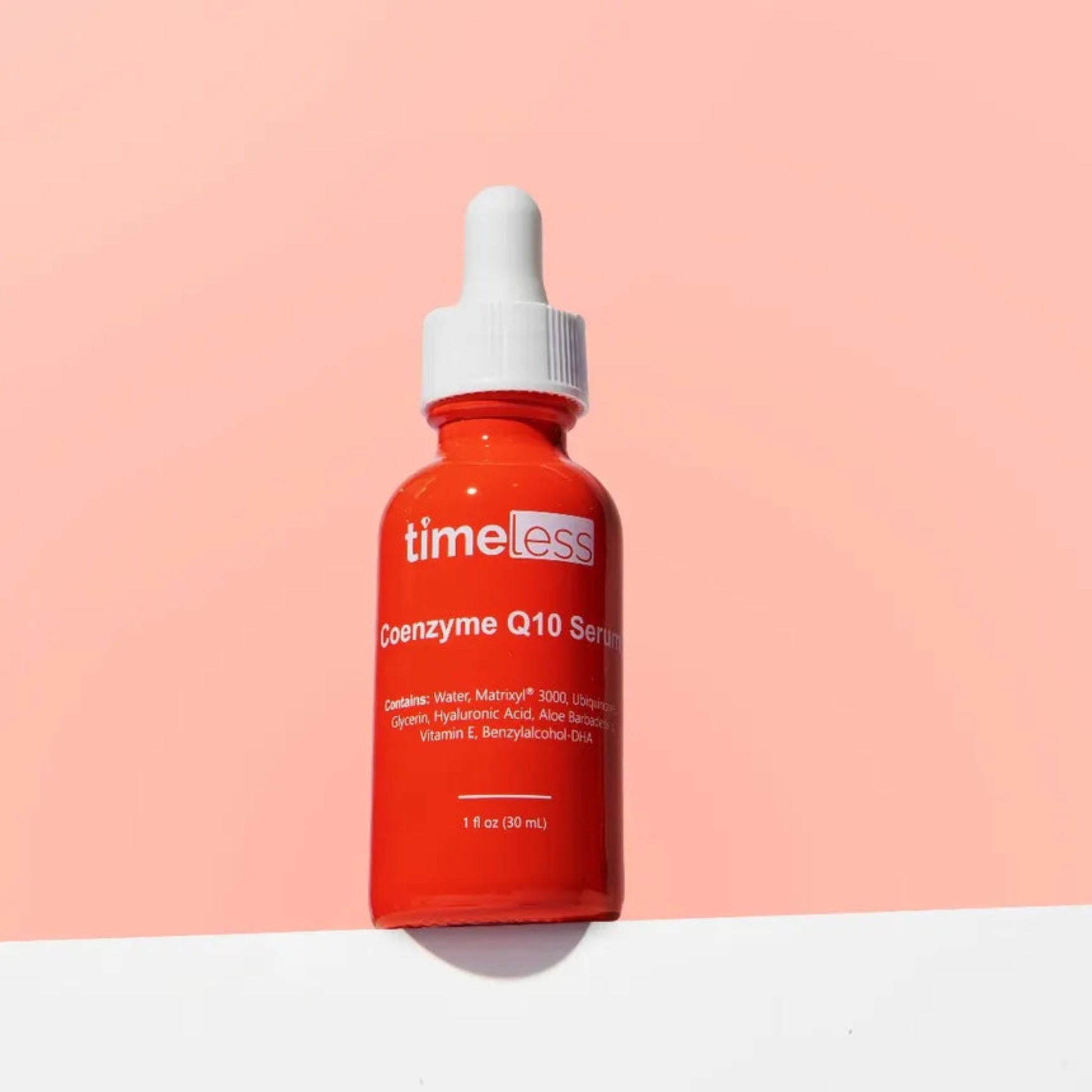 Red serum bottle with white cap labeled 'timeless' on a pink background