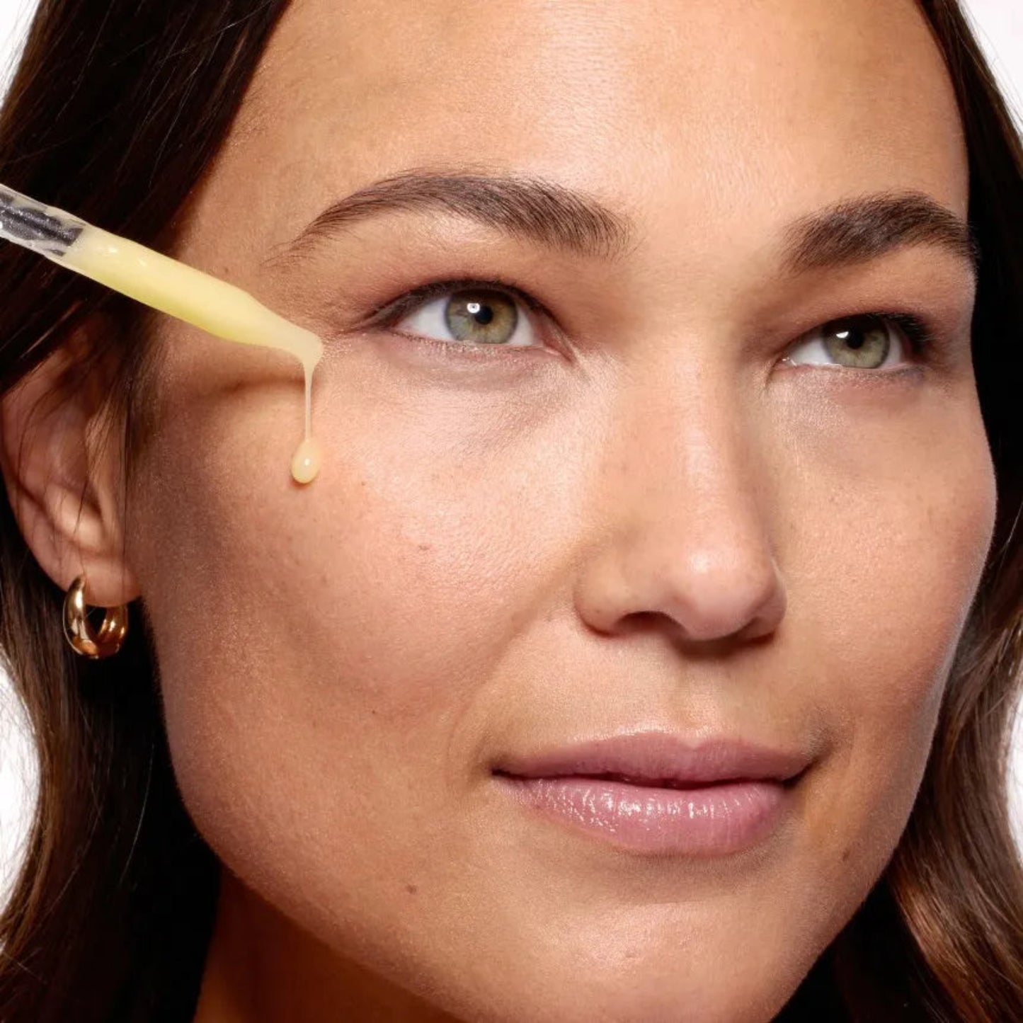 Close-up of a woman applying a dropper of cream to her face.