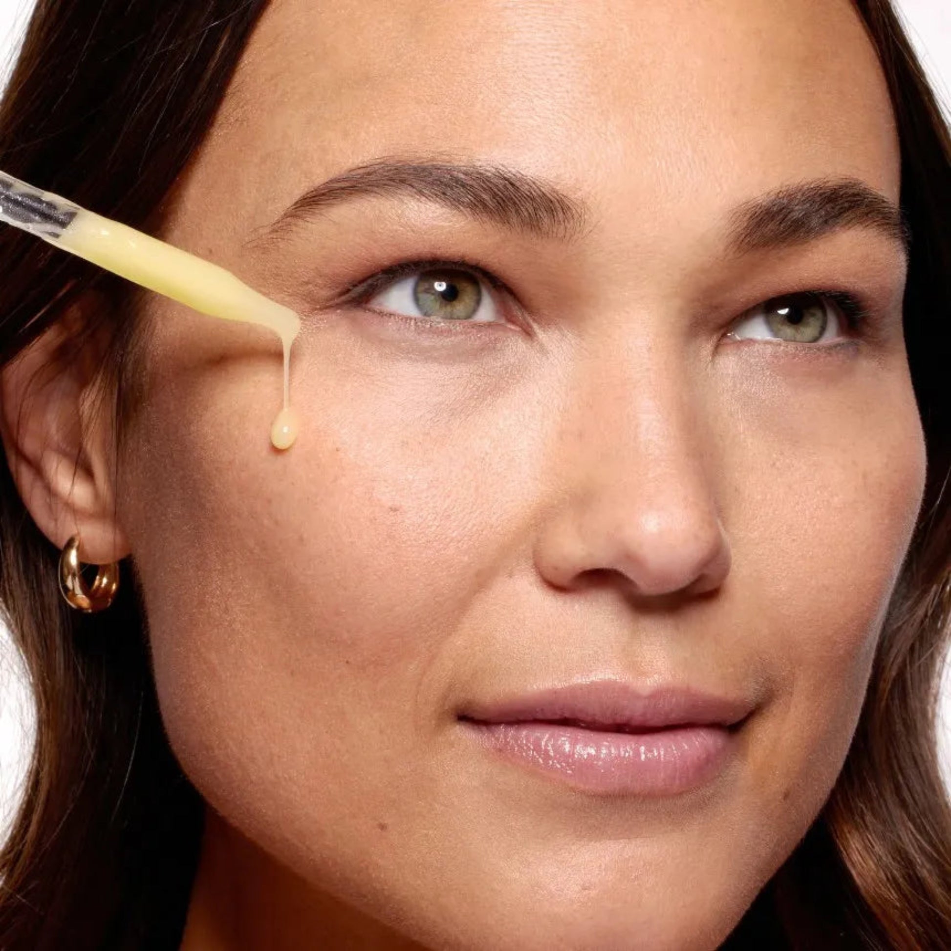 Close-up of a woman applying a dropper of cream to her face.